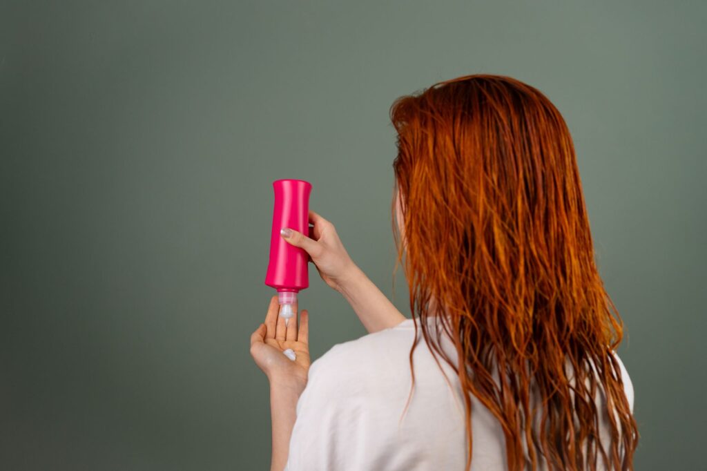 Femme rousse de dos vaporisant un soin sur ses longueurs
