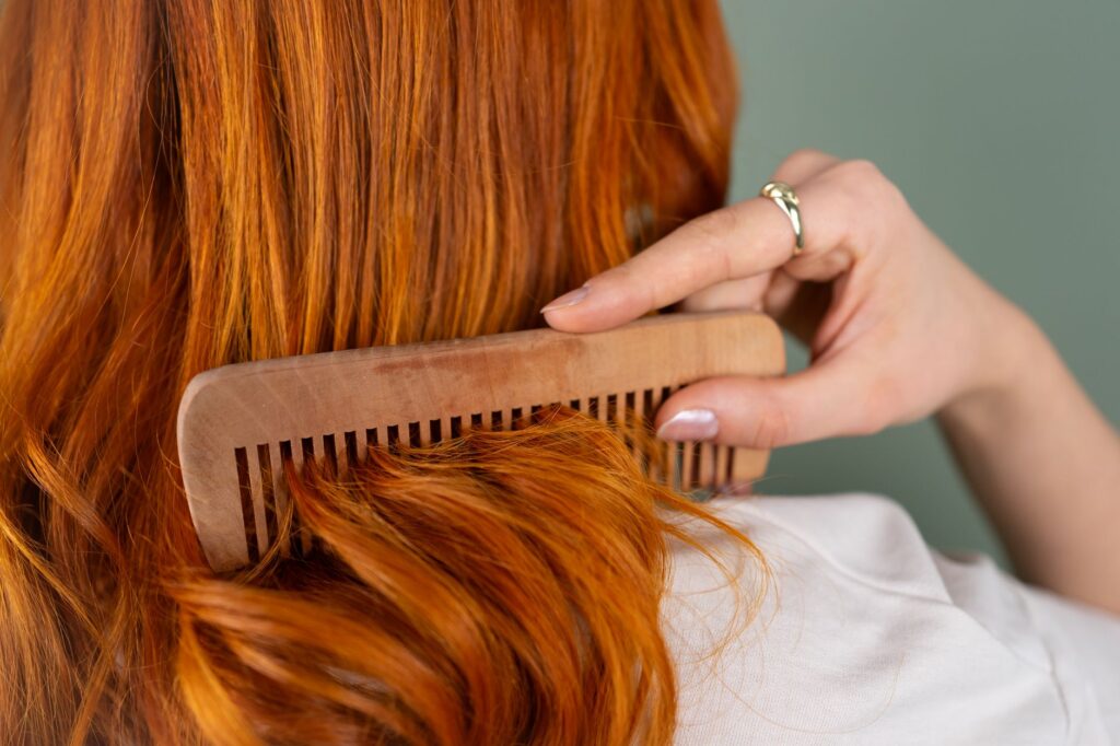 Peigne en bois passé dans de longs cheveux roux brillants