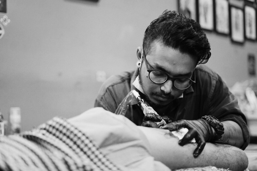 Tatoueur ganté au travail sur un bras, photographie en noir et blanc