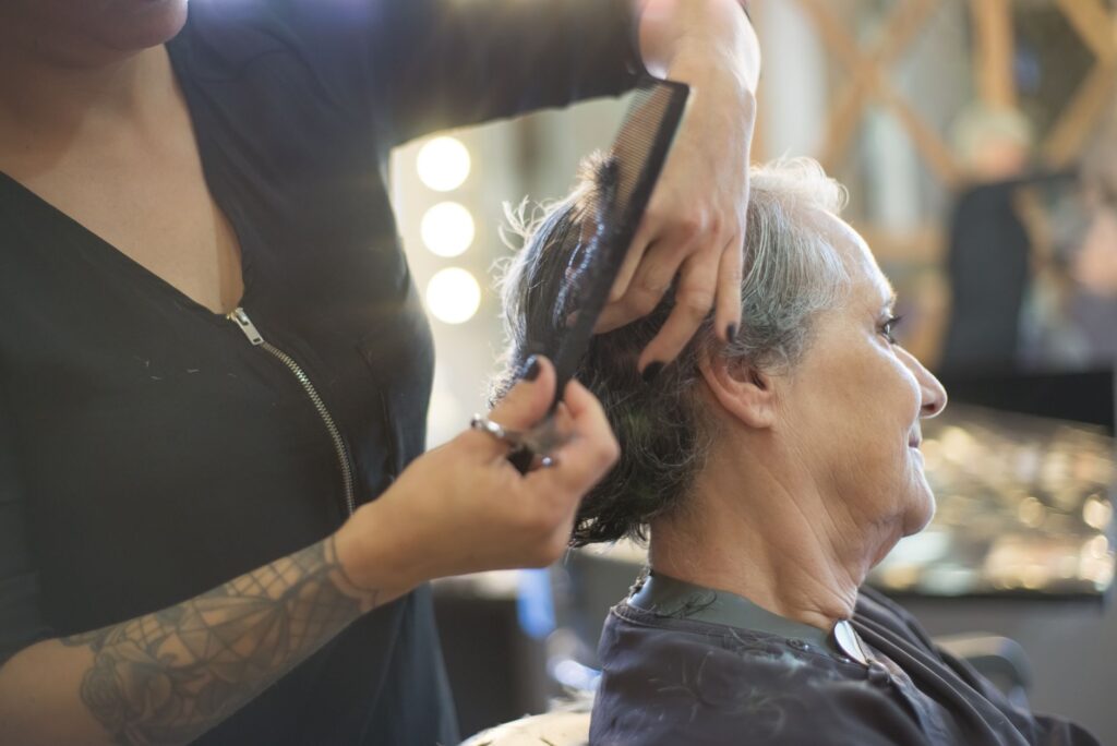 Coiffeur travaillant les cheveux courts d'une cliente sénior en salon