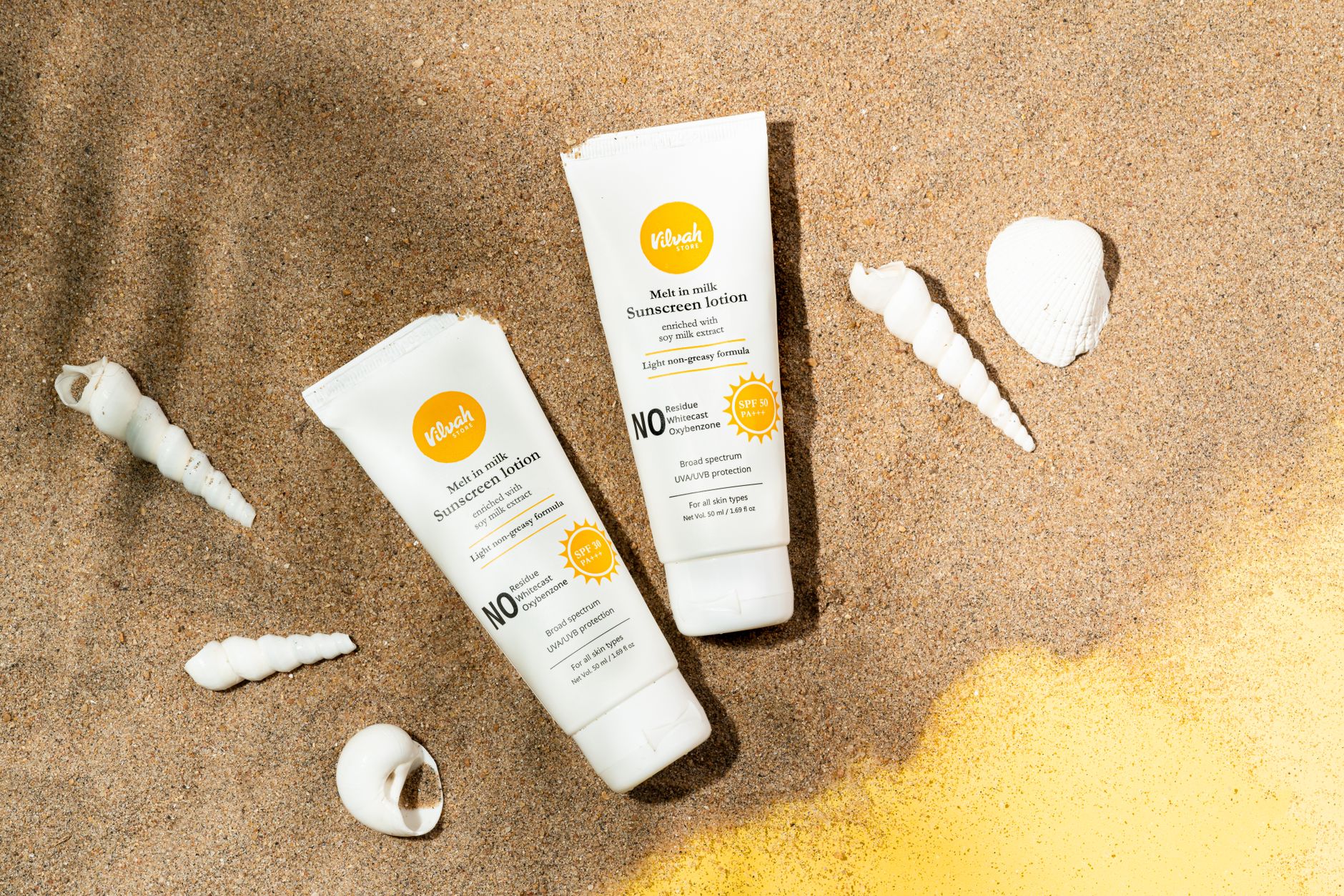 Deux tubes de crème solaire posés sur le sable avec des coquillages