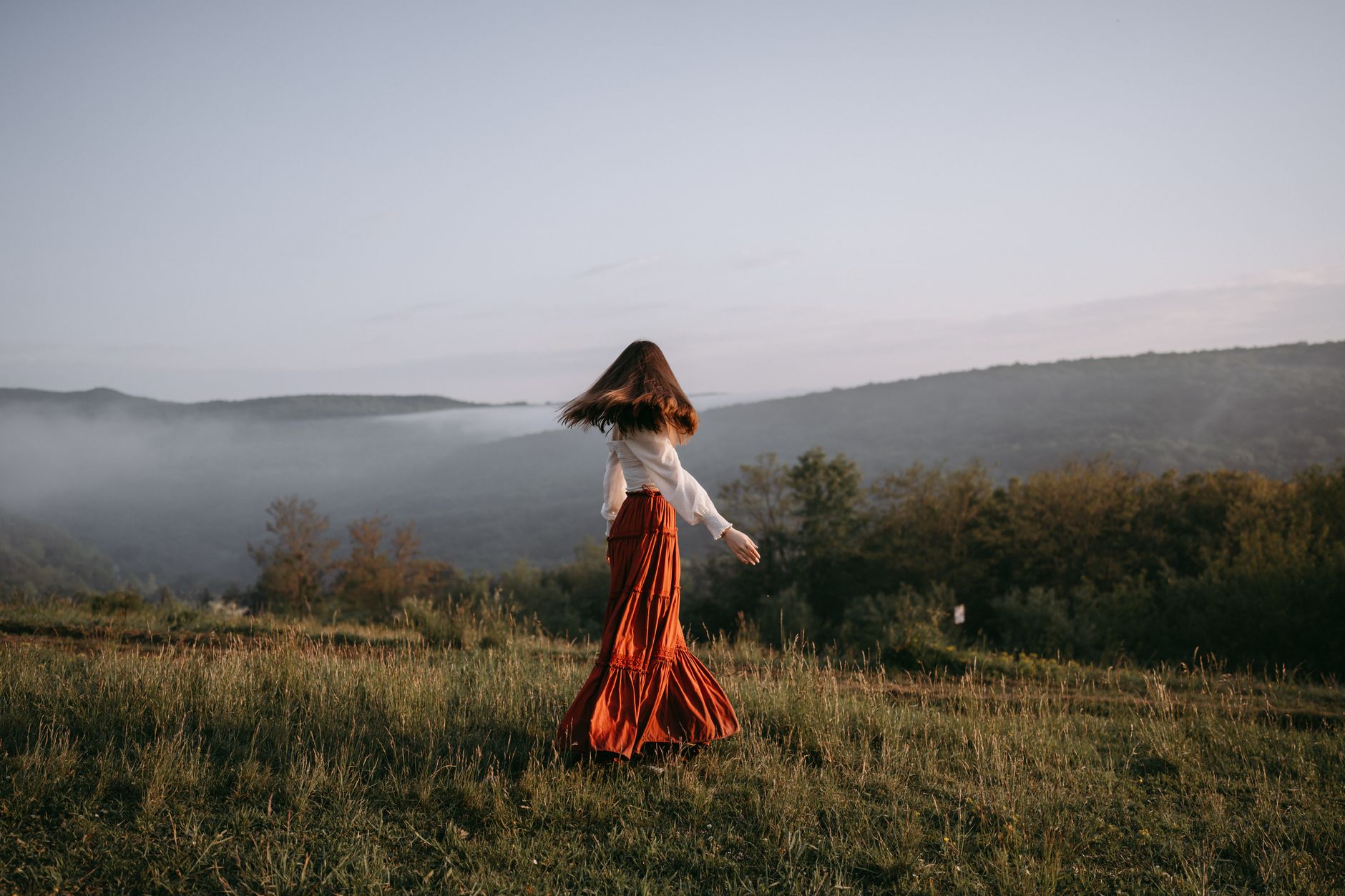 Femme en jupe longue fluide marchant dans un pré au petit matin
