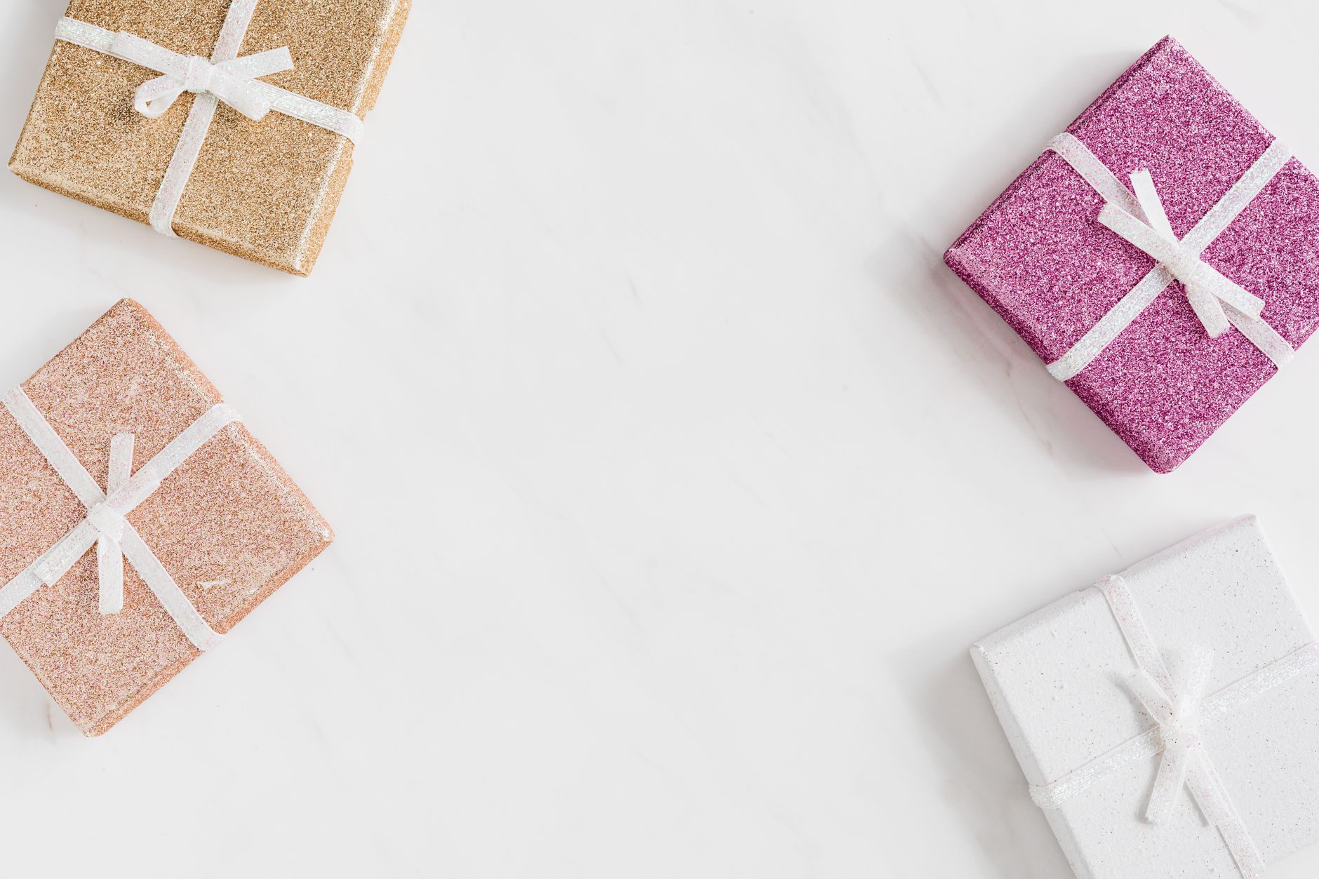 Petits paquets cadeaux pailletés rose et cuivre posés sur fond blanc